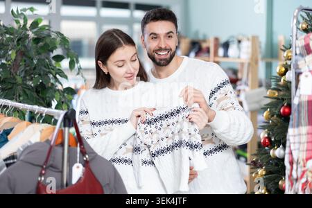 Couple marié choisir des pulls sur fond d'arbre de Noël dans le magasin de vêtements Banque D'Images