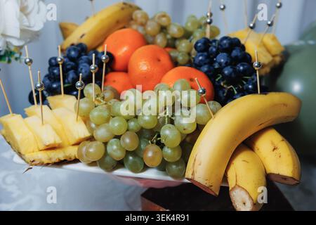 Plateau de fruits frais avec bananes, raisins, oranges et tranches d'ananas Banque D'Images