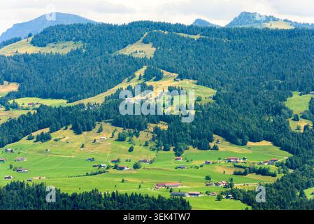 Une vue panoramique sur une vallée verdoyante dans les Alpes suisses pendant la journée. La scène présente des prairies vallonnées parsemées de chal en bois traditionnel Banque D'Images