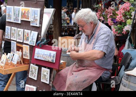 Paris, France - 9 août 2024 : artiste de rue parisien âgé peignant des aquarelles et vendant des souvenirs faits à la main sur un marché en plein air de par Banque D'Images