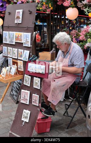 Paris, France - 9 août 2024 : peintre de rue âgé créant des aquarelles et vendant des peintures faites à la main sur un marché en plein air animé à Paris Banque D'Images
