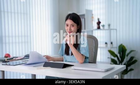 Femme asiatique portant un casque fournissant un service de consultation à distance dans l'espace de travail moderne lumineux de bureau à domicile avec tablette Banque D'Images