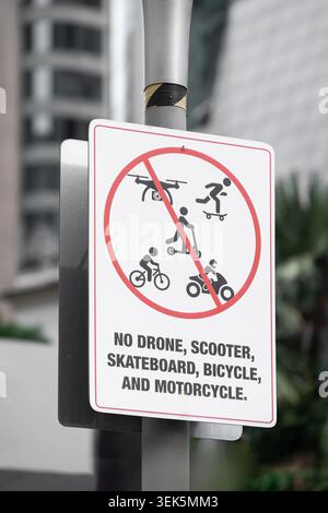 Un panneau de sécurité de rue monté sur un poteau, indiquant l'utilisation interdite de drones, scooters, planches à roulettes, vélos et motos dans la zone, placé contre Banque D'Images