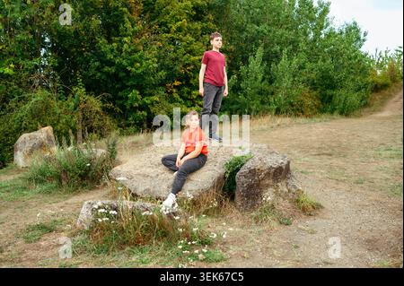 Enfant fille assise sur des rochers tandis que frère adolescent debout Banque D'Images