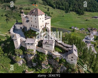 Vue aérienne du Schloss Tarasp sur une colline rocheuse entourée de prairies verdoyantes, de forêts denses et d'un petit lac Scuol, Graubunden, Suisse. Banque D'Images