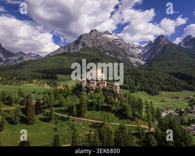 Vue aérienne du Schloss Tarasp perché sur une colline rocheuse entourée de forêts verdoyantes et de prairies avec les Alpes suisses en arrière-plan Scuol, Graubu Banque D'Images