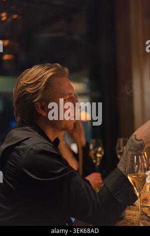 Homme blond élégant dans le profil assis au bar avec verre à vin, Paris Banque D'Images