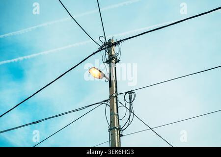 Poteau de puissance électrique transportant des câbles aériens et lampadaire incandescent sous ciel clair, scène de distribution de technologie et d'énergie, mise au point sélective Banque D'Images