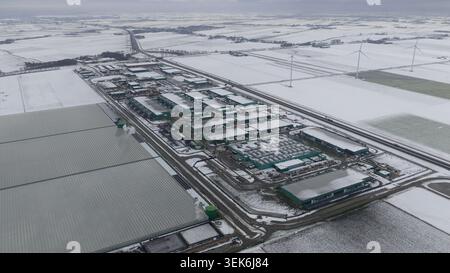 Vue aérienne d'un grand complexe de centres de données industriels et de serres entourées de champs enneigés et d'éoliennes Middenmeer, Hollande du Nord, N. Banque D'Images