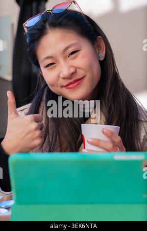 Portrait vertical femme asiatique heureuse donnant les pouces au café en plein air avec tablette Banque D'Images