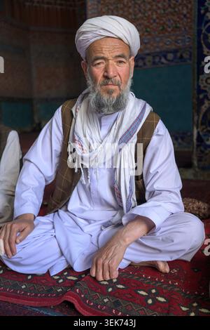Homme portant des vêtements traditionnels assis sur un tapis à motifs à l'intérieur d'une mosquée Banque D'Images