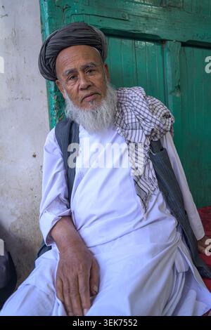 Homme aîné afghan avec une longue barbe blanche assis, regardant attentivement la caméra. Banque D'Images