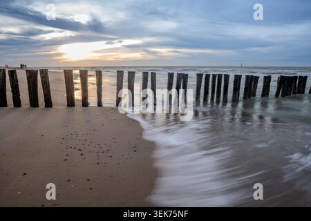 Les poteaux en bois forment une ligne dans le sable, avec les vagues de l'océan qui coulent doucement autour d'eux et reculent sur la plage. De Westkapelle, Zélande, pays-Bas Banque D'Images