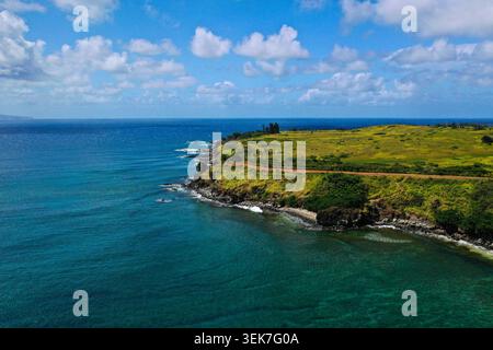 Une vue aérienne à couper le souffle de Maui, Hawaï, mettant en valeur des falaises verdoyantes côtières, une route sinueuse et le vaste océan bleu sous un ciel légèrement nuageux. Banque D'Images
