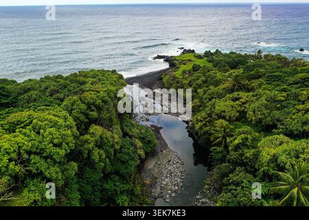 Une vue aérienne d'un paysage côtier verdoyant avec une superbe plage de sable noir, un ruisseau sinueux et une végétation tropicale vibrante à Maui, Hawa Banque D'Images