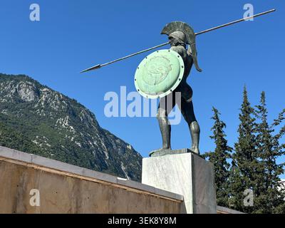 Statue du roi Spartiate Leonidas tenant une lance et un bouclier à Delphes, en Grèce, avec des montagnes s'élevant en arrière-plan sous un ciel bleu clair. Banque D'Images