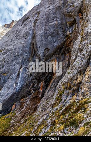 Une vue spectaculaire sur une face de montagne escarpée et rocheuse avec un petit ruisseau d'eau descendant en cascade. La roche grise est texturée et altérée, avec des taches de Banque D'Images