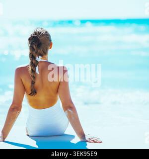 Jeune femme assise au bord de mer. Vue arrière Banque D'Images