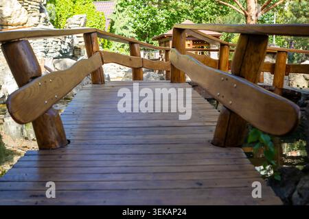 Pont de jardin en bois sur l'étang dans un parc rustique passerelle entouré d'arbres et de pierres Banque D'Images