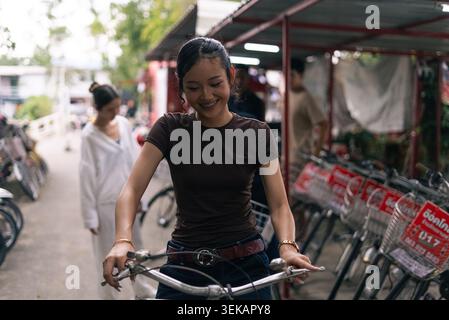 Jeune femme asiatique souriante, profitant de la vie sur le campus tout en poussant un vélo Banque D'Images