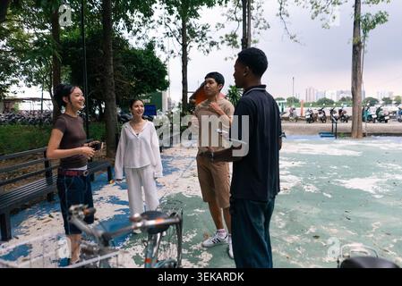 Jeunes adultes diversifiés ayant des discussions animées et communiquant en plein air dans un parc urbain Banque D'Images