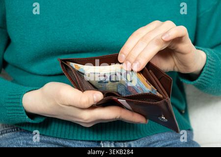Femme vérifiant les billets de banque en papier dans le portefeuille brun de près. Banque D'Images
