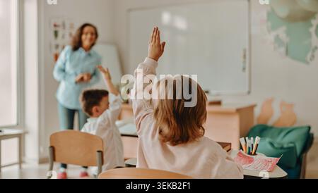 Les élèves de l'école primaire caucasienne levant la main pendant la leçon avec un professeur en classe Banque D'Images