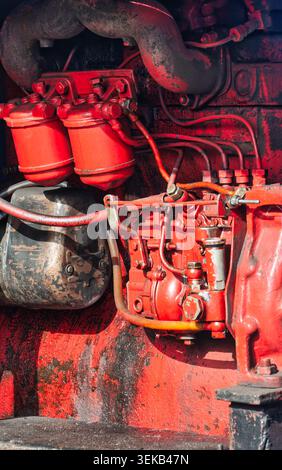 gros plan présentant les composants mécaniques, les doubles filtres à carburant et la tuyauterie complexe d'un vieux moteur diesel industriel rouge. Banque D'Images