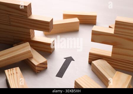 Mur en bois effondré fait de blocs et flèche de papier sur la table, gros plan. Surmonter les obstacles Banque D'Images