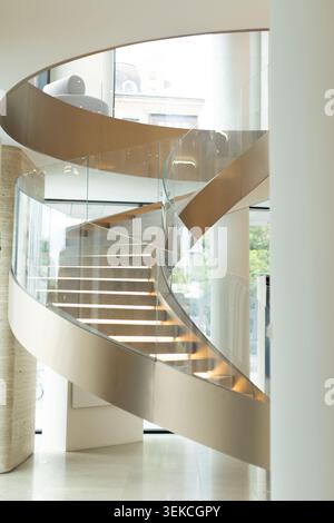 Vue imprenable sur un escalier moderne en pierre à spirale à l'intérieur d'un hall lumineux. Les marches incurvées sont dotées de bandes lumineuses LED intégrées sous le bord avec gl élégant Banque D'Images
