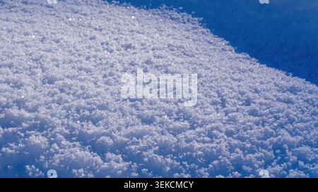 Gros plan extrême de neige blanche pure révélant sa texture cristalline pétillante et glacée sous la lumière du soleil. Idéal pour les milieux hivernaux et de vacances. Banque D'Images