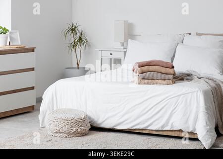 Pile de pulls tricotés sur le lit dans une chambre élégante Banque D'Images