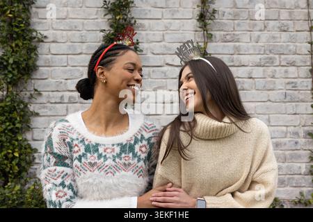 Diverses amies féminines assis près du mur de briques grises, portant des bandeaux festifs et des chandails Banque D'Images