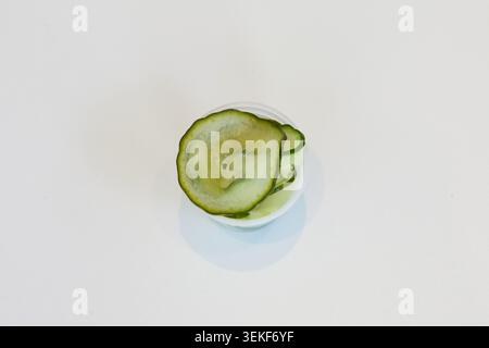 Gros plan de cornichon de concombre tranché dans une petite casserole en plastique sur un fond blanc pour les ingrédients du bol de poke. Banque D'Images