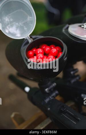 Gros plan de la trémie de marqueur de paintball remplie de balles de paintball rouges avant le match en plein air. Équipement de tir récréatif préparé pour la compétition en équipe et Banque D'Images