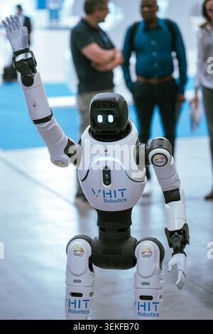 Une vue rapprochée d'un robot humanoïde VHIT Robotics levant son bras droit dans un geste de salutation lors d'une présentation d'exposition, avec l'atten de la foire commerciale Banque D'Images