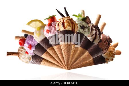 Cônes de crème glacée assortis colorés disposés en éventail avec différentes saveurs, fruits, garnitures de chocolat, noix et gaufrettes isolés sur un bac blanc Banque D'Images