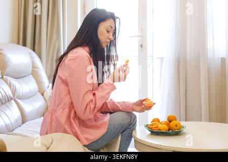 Portrait d'une femme mangeant des mandarines à la maison Banque D'Images