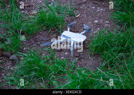 Une photographie en gros plan à grand angle montrant un quadcopter de drone compact blanc moderne debout sur un sol en terre battue entouré d'herbe verte fraîche Banque D'Images
