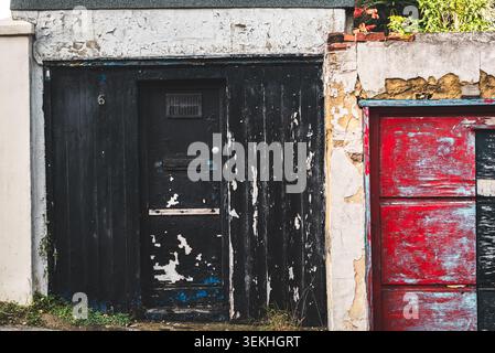 Une vue rapprochée de deux portes adjacentes, une noire et une rouge, mettant en valeur leurs surfaces endommagées et leur peinture écaillée Banque D'Images