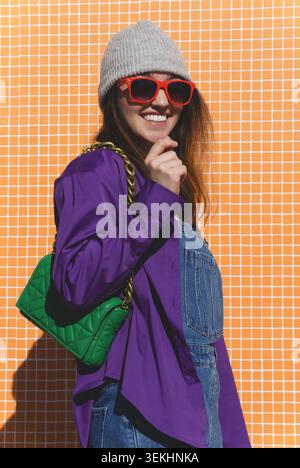 Femme souriante posant dans des vêtements colorés avec son sac à main sur un fond vibrant Banque D'Images