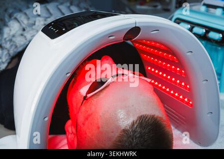 Lors d'un rendez-vous de cosmétologie, une personne reçoit une thérapie à la lumière rouge pour le traitement de la peau. Le dispositif est positionné sur le visage, fournissant e ciblé Banque D'Images