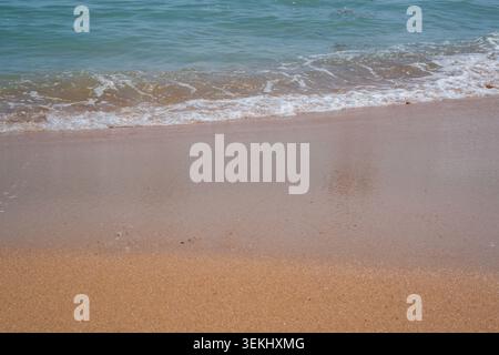 De douces vagues se jettent sur une plage de sable à Sharm El Sheikh Egypte avec de l'eau claire le long du rivage de la mer Rouge en plein jour. Style de vie de station balnéaire. Banque D'Images