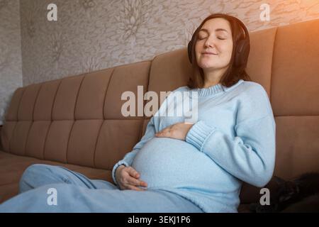 Femme enceinte se reposant sur un canapé à la maison en plein soleil Banque D'Images