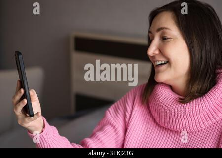 Femme enceinte souriant tout en tenant un smartphone à l'intérieur Banque D'Images