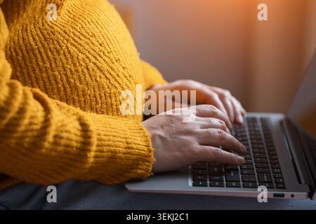 Femme enceinte tapant sur un ordinateur portable tout en tenant son ventre Banque D'Images