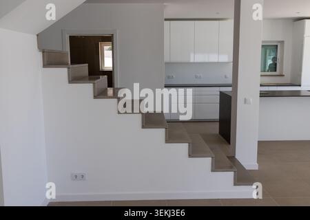 Un intérieur contemporain présente un escalier flottant menant à une cuisine lumineuse et ouverte avec des armoires blanches et des comptoirs sombres Banque D'Images