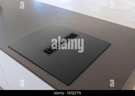 Une table de cuisson à induction intégrée élégante dotée d'un système de ventilation central, parfaitement intégrée dans un comptoir îlot de cuisine en pierre sombre Banque D'Images