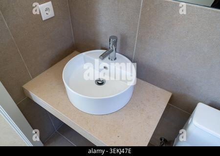 Une salle de bains épurée et contemporaine avec un lavabo blanc rond, un robinet chromé élégant et un comptoir texturé Banque D'Images