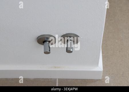 Vue rapprochée de deux crochets à serviettes cylindriques chromés élégants installés sur un plafond blanc texturé, adjacent à des murs carrelés beiges Banque D'Images